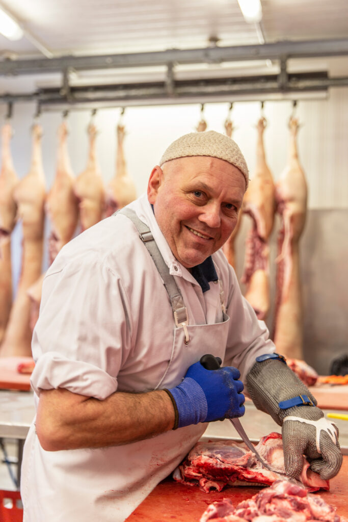 Ein lächelnder Metzger steht an seiner Station in der Bio-Hoffleischerei und schneidet das Bio-Fleisch von Vorwerk Podemus.